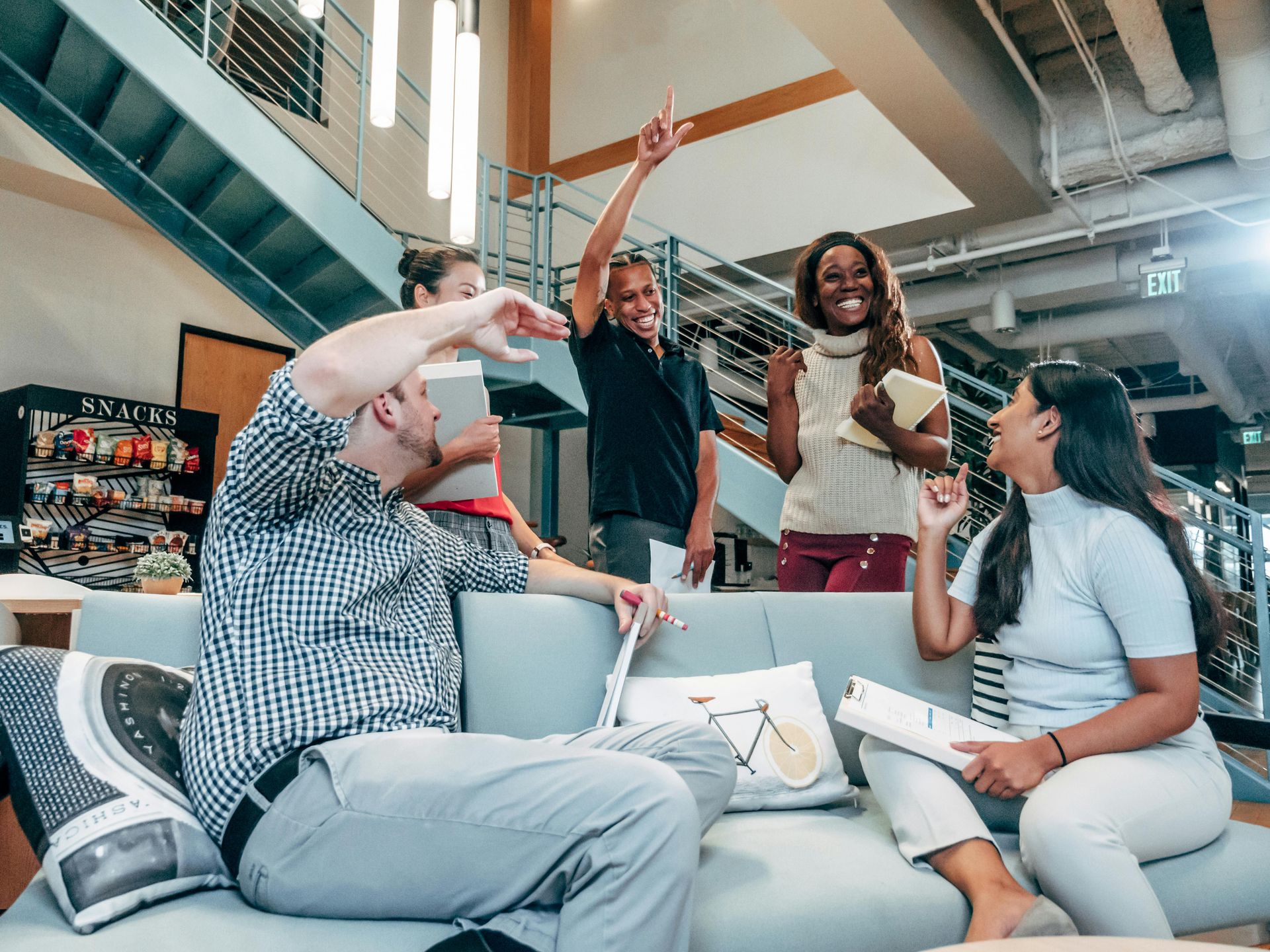 Group of diverse people celebrating in an office lounge. One man raises a fist, others cheer and smile.