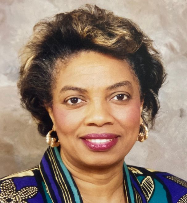 Woman with dark skin, wearing gold earrings and a patterned top, smiling.