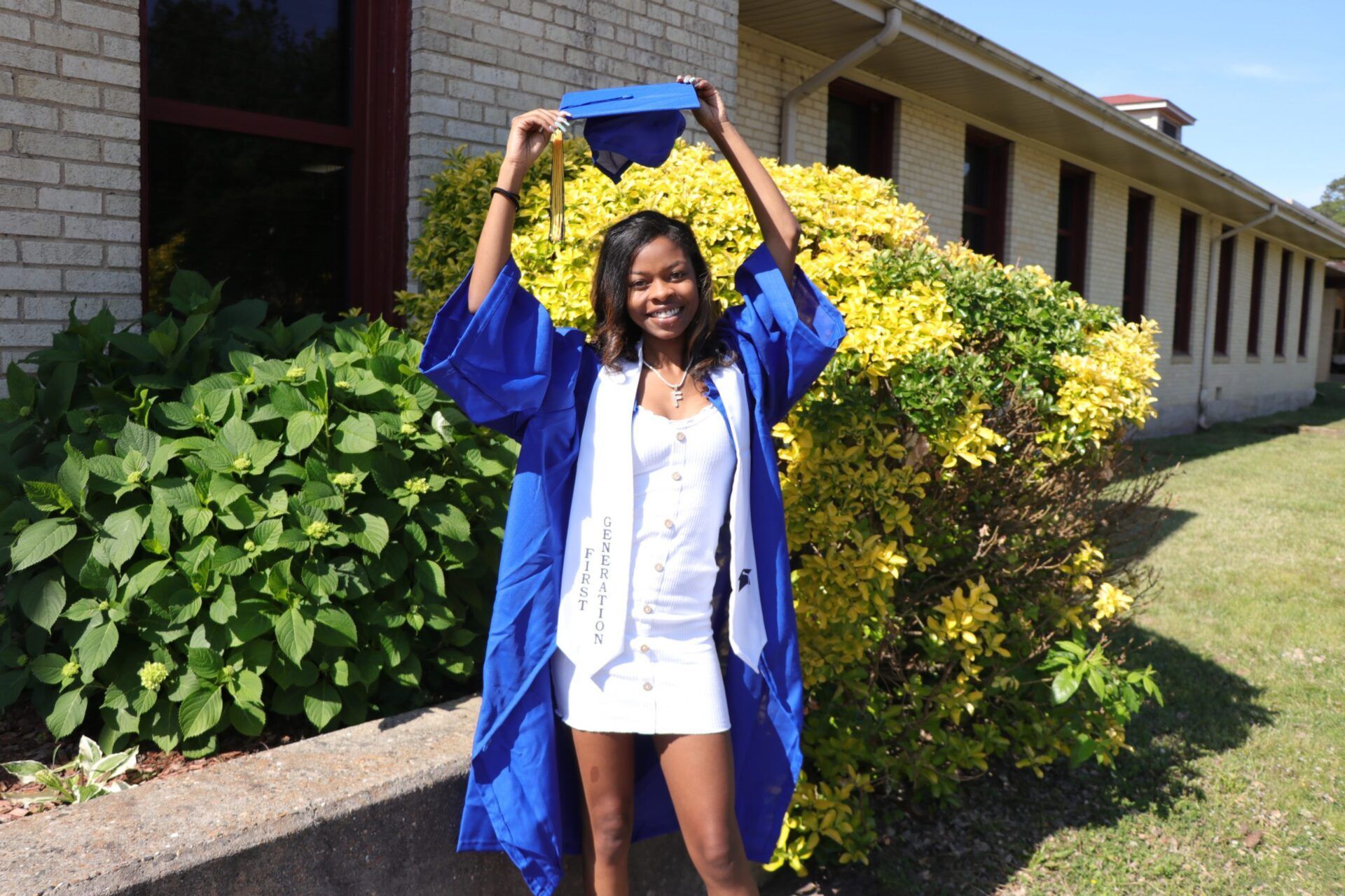 A woman in a graduation cap and gown is holding her cap in the air