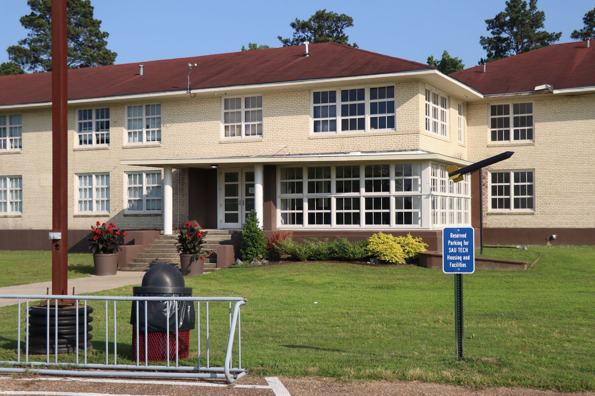 Two-story beige building with a brown roof and white-framed windows. A grassy lawn in front, a sign, and a fire hydrant.