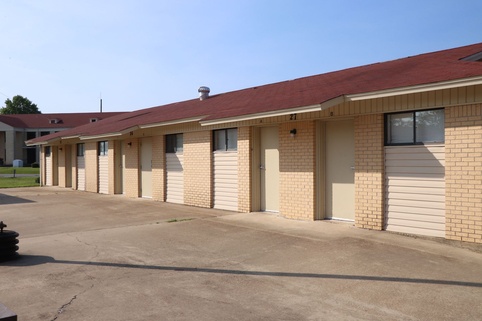 Row of tan brick motel rooms with brown roof, concrete drive.