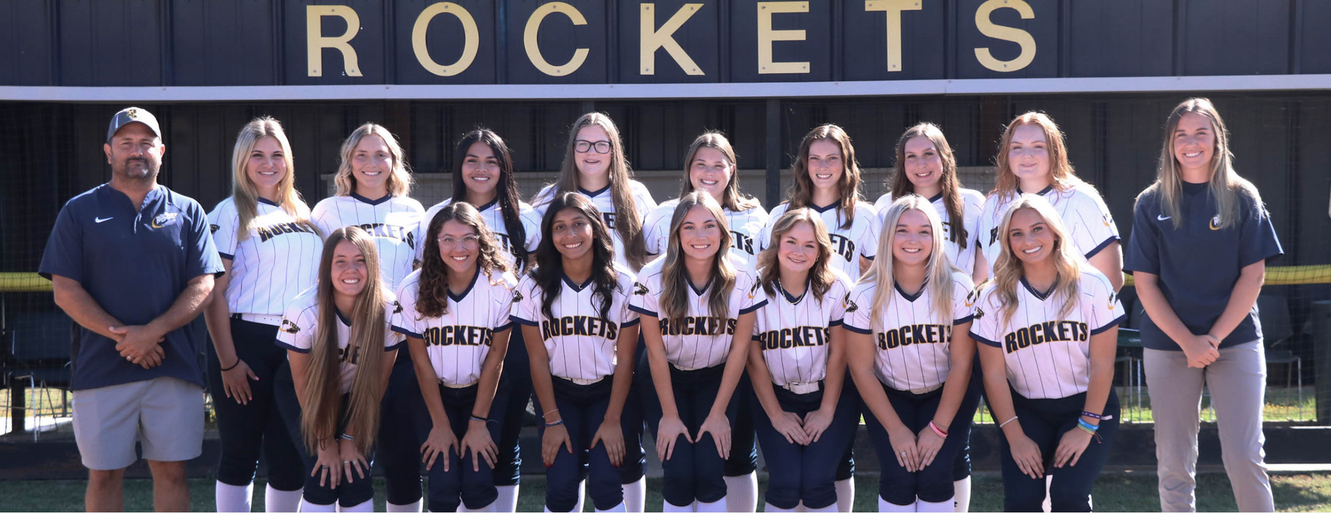A softball team is posing for a picture in front of a sign that says rockets.