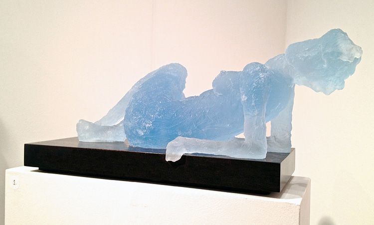 A blue glass sculpture of a woman laying down on a black base