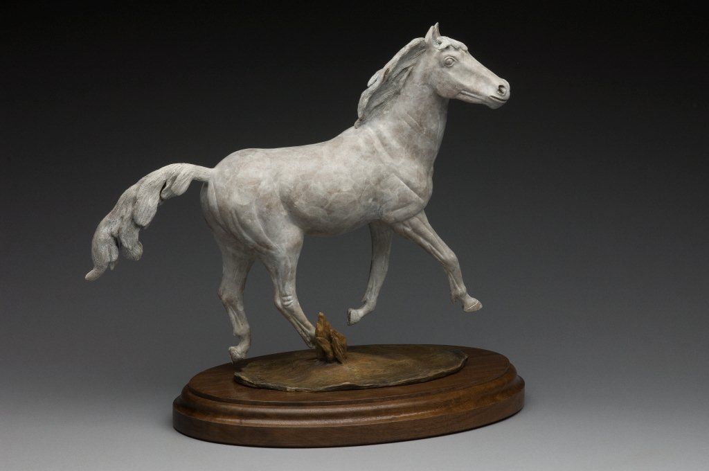 A statue of a white horse running on a wooden base.