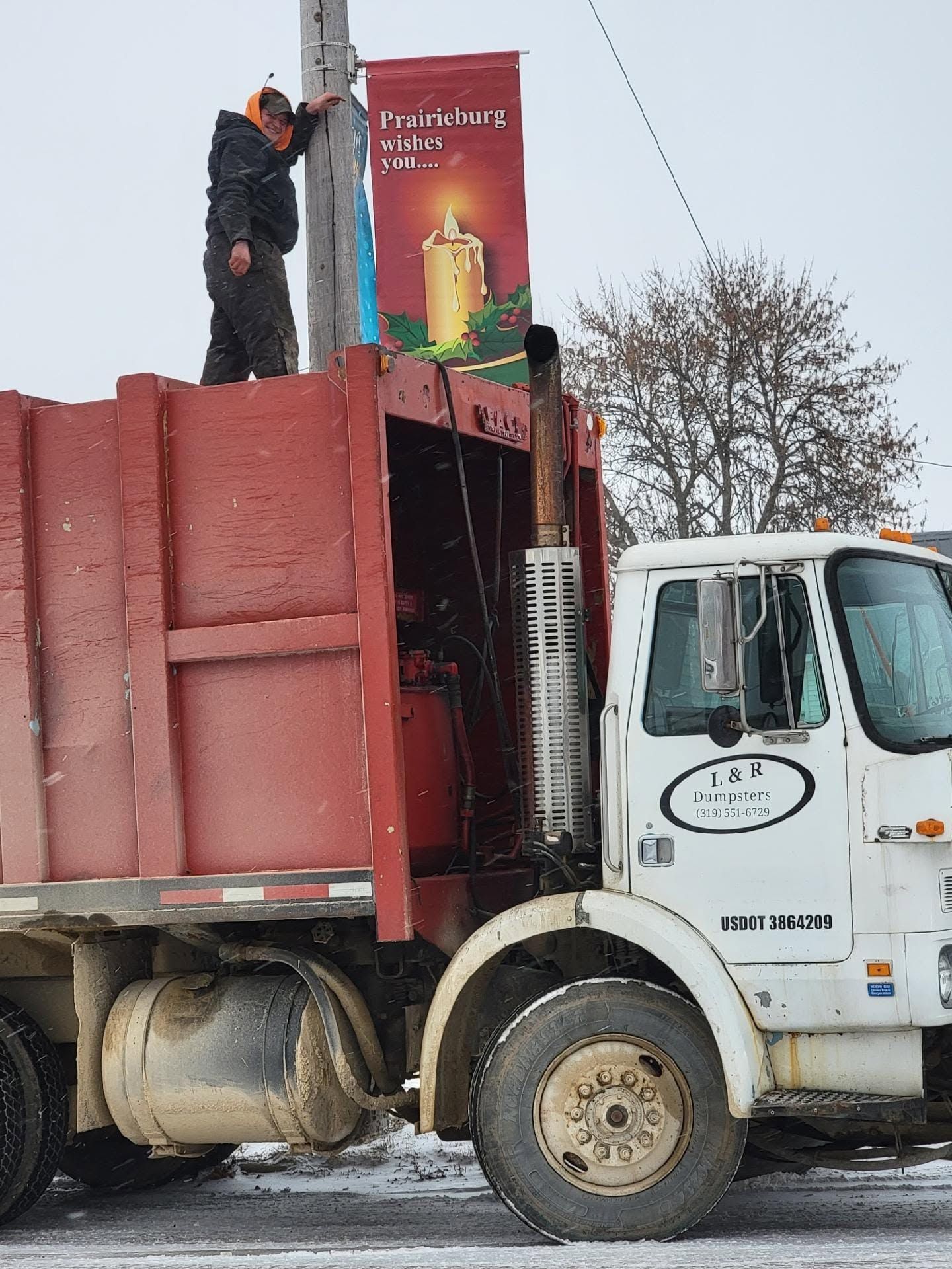 Man standing on red dump truck bed near a billboard, with white cab in an outdoor lot.