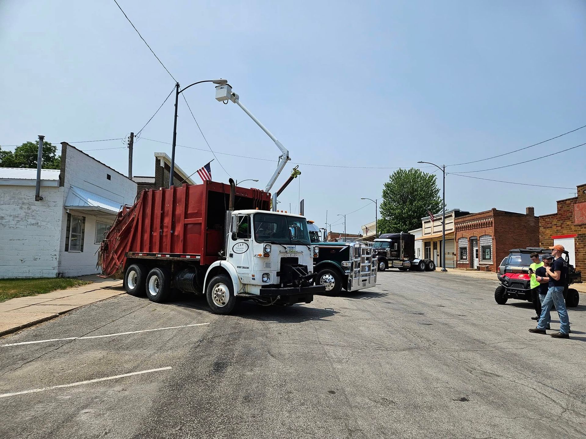 Two utility trucks on a street, with workers nearby and a red truck lifting overhead wires.