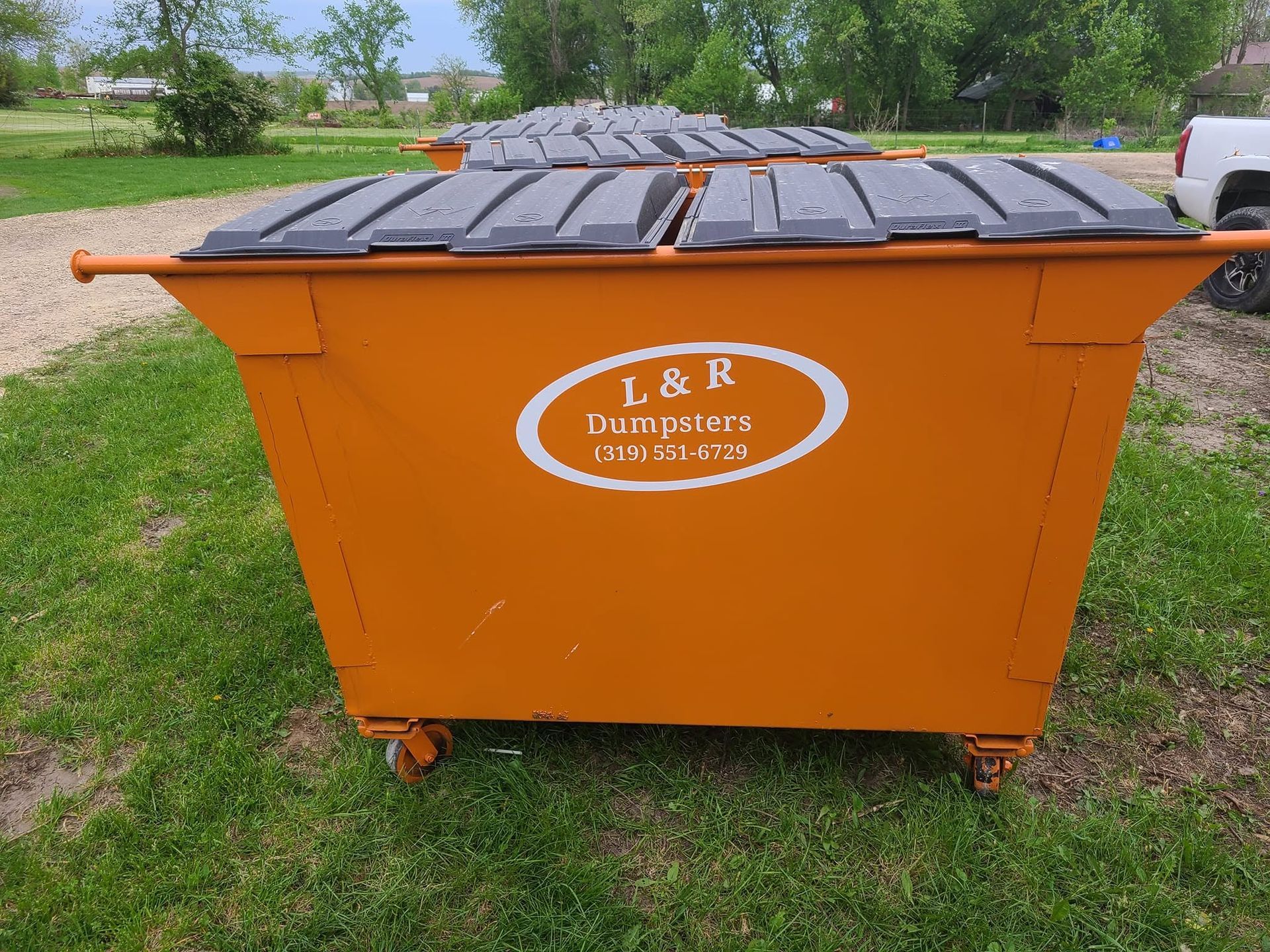 Orange dumpster with black lid in a grassy outdoor area