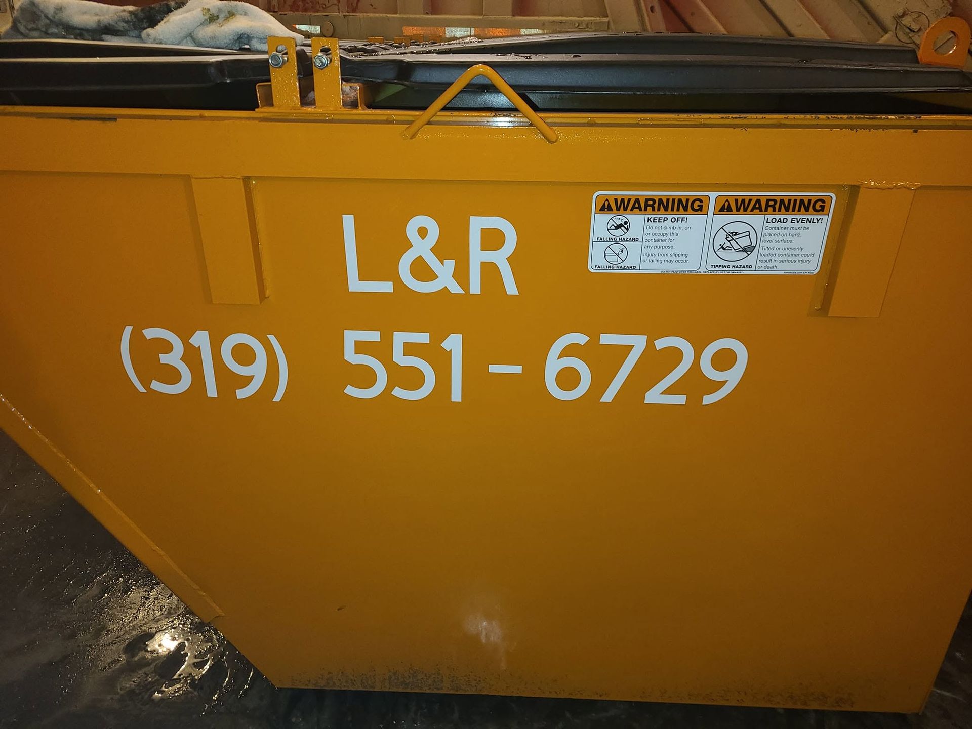 Orange dumpster with “L&R” and phone number (319) 551-6729 painted on the side.