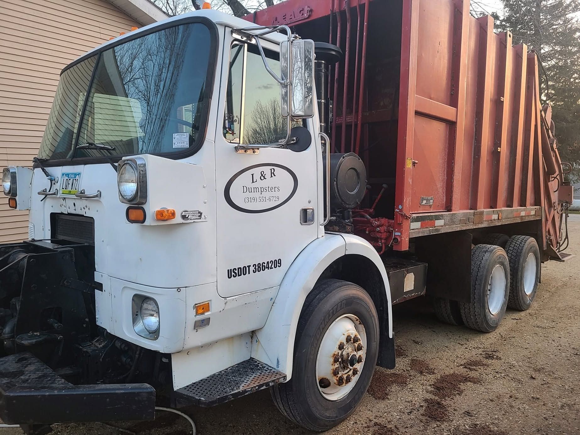 White cargo truck with a red container parked on a dirt lot beside a brick building