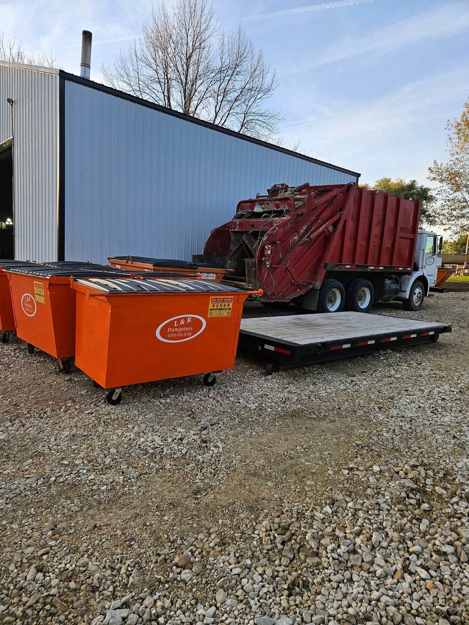 Red truck and orange dumpster trailers on a gravel lot beside a white metal building