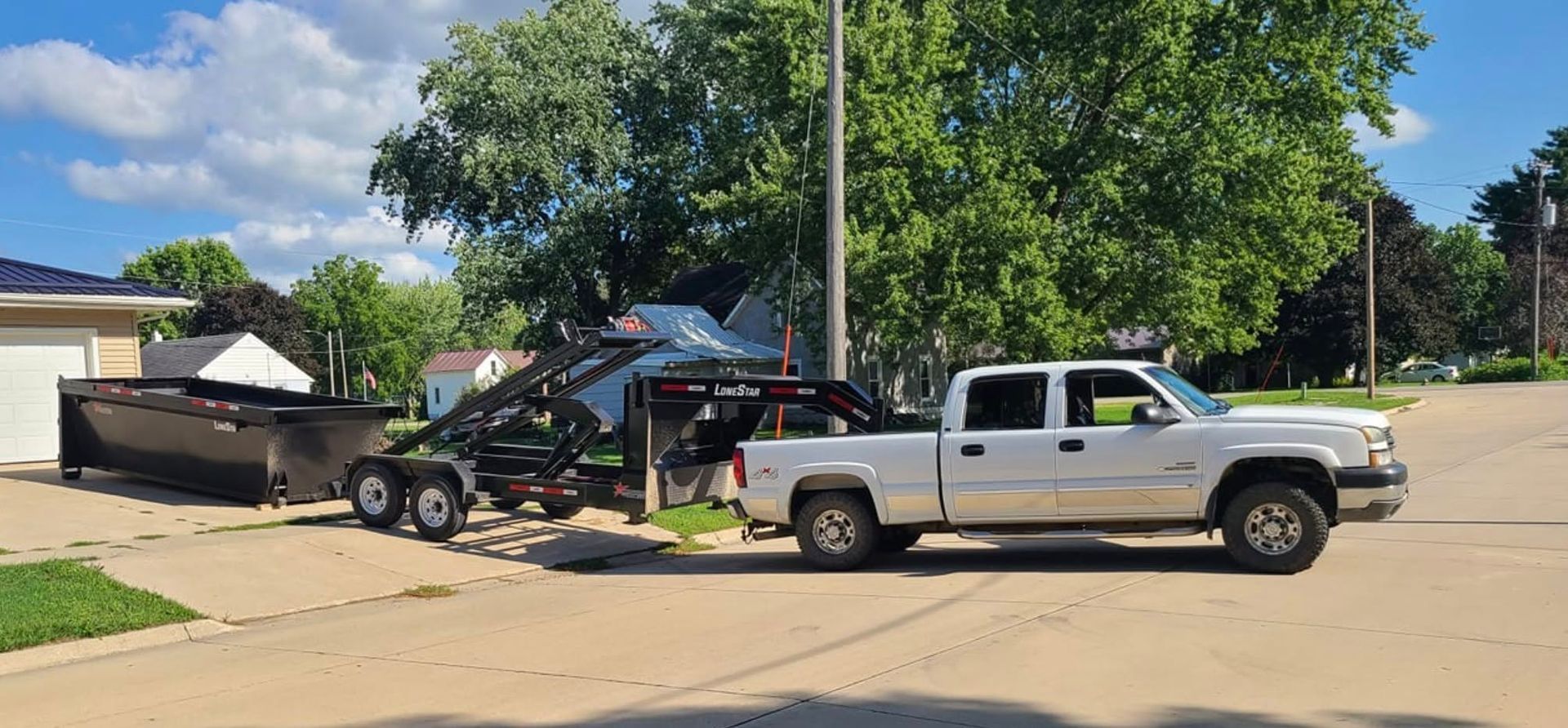 Two tow trucks loading a damaged car on a residential street under trees