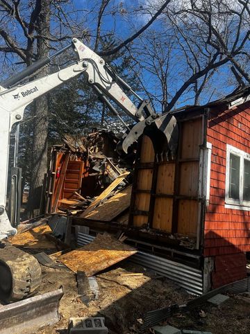Excavator demolishing a house, tearing into a brick wall and exposing the interior.