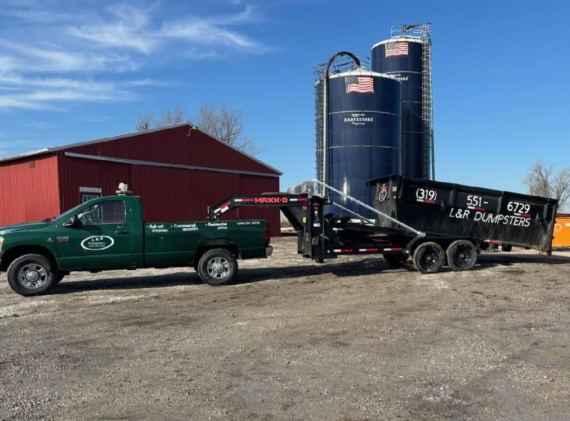 Green pickup and black trailer parked beside blue silos and a red barn on a farm.