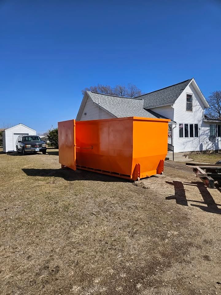 Bright orange dumpster in a yard beside a white house under a blue sky