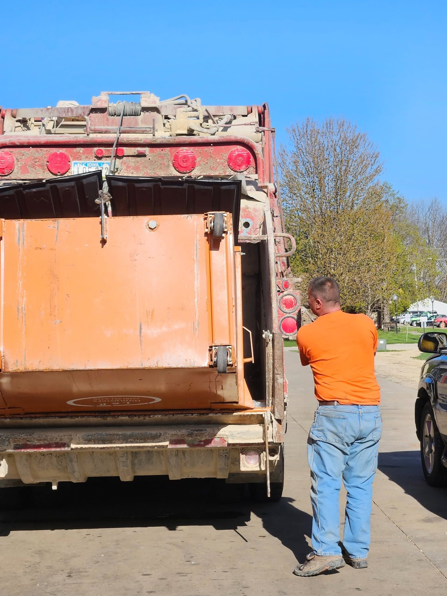 Man in orange shirt pushing a large orange dumpster at a roadside.