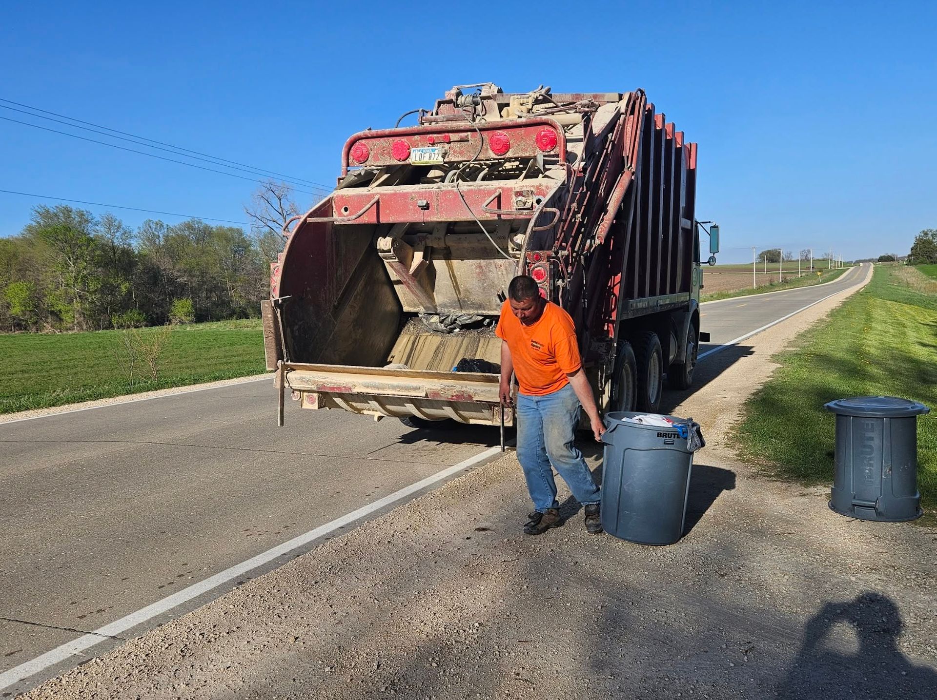 Garbage truck stopped on a roadside as a worker empties bins into it on a sunny day