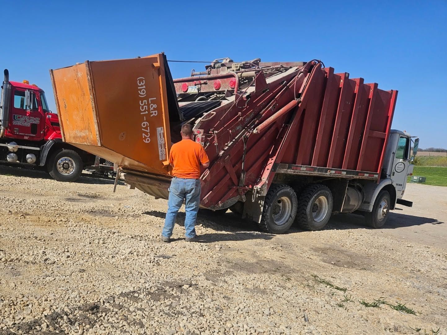 Overturned red semi trailer on gravel lot as worker in orange shirt inspects it