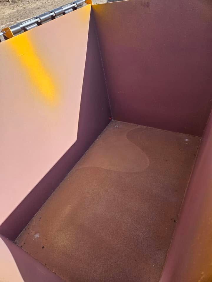 Purple-walled corner of an empty bin with a dusty brown floor and yellow sunlight streaks