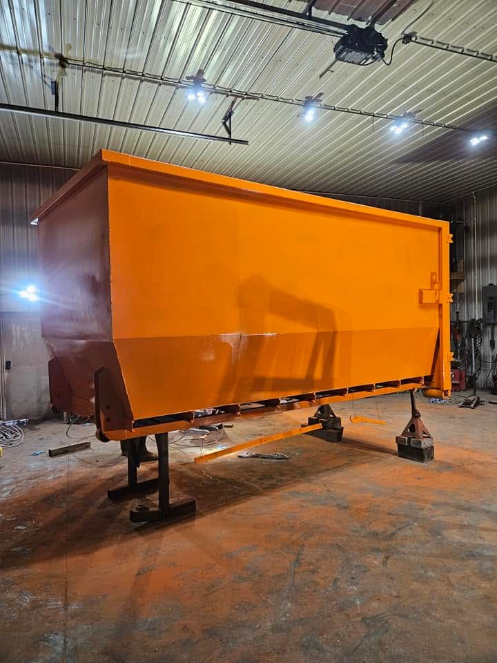 Bright orange industrial trailer or container on jacks inside a workshop under overhead lights