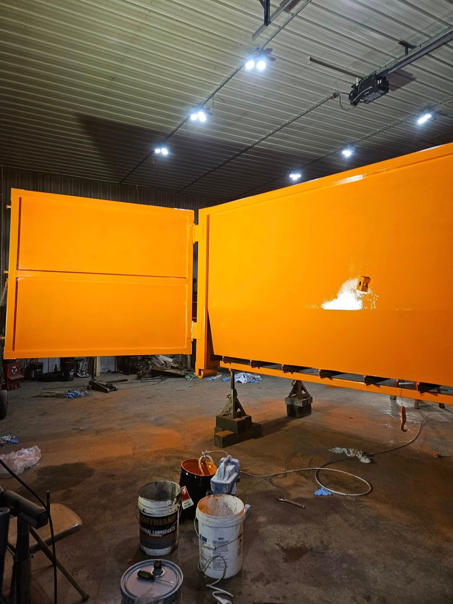 Orange stage panels in a dim room, with lights overhead and paint supplies on the floor