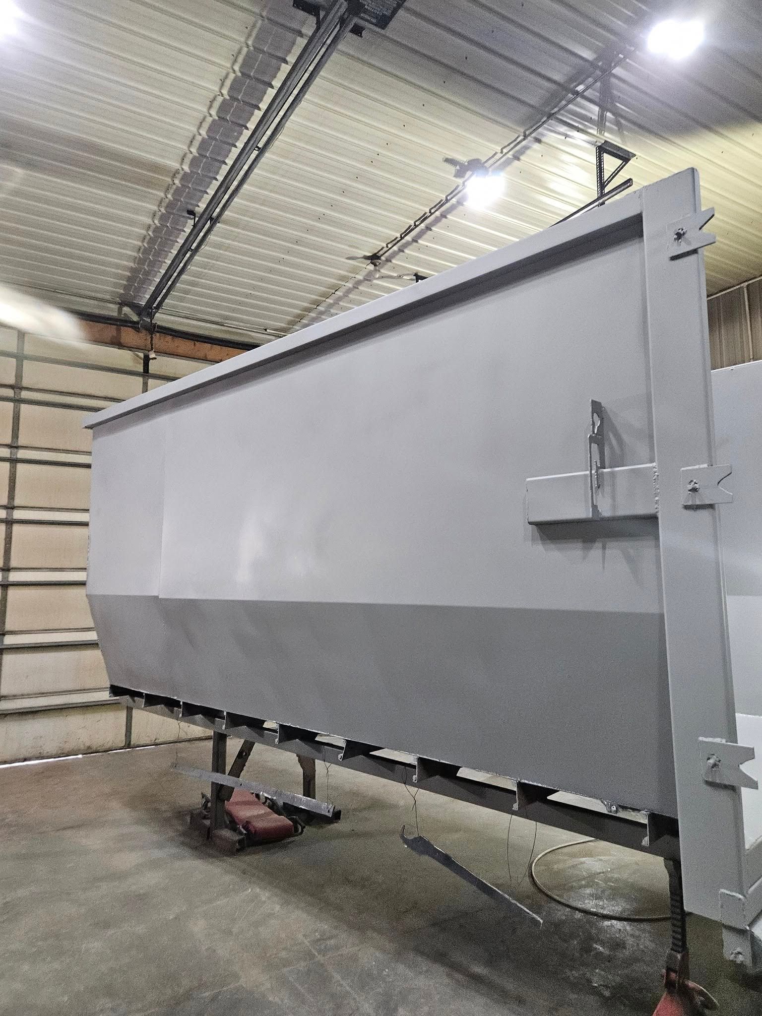 Large gray industrial metal panel or hopper on stands inside a warehouse workshop.