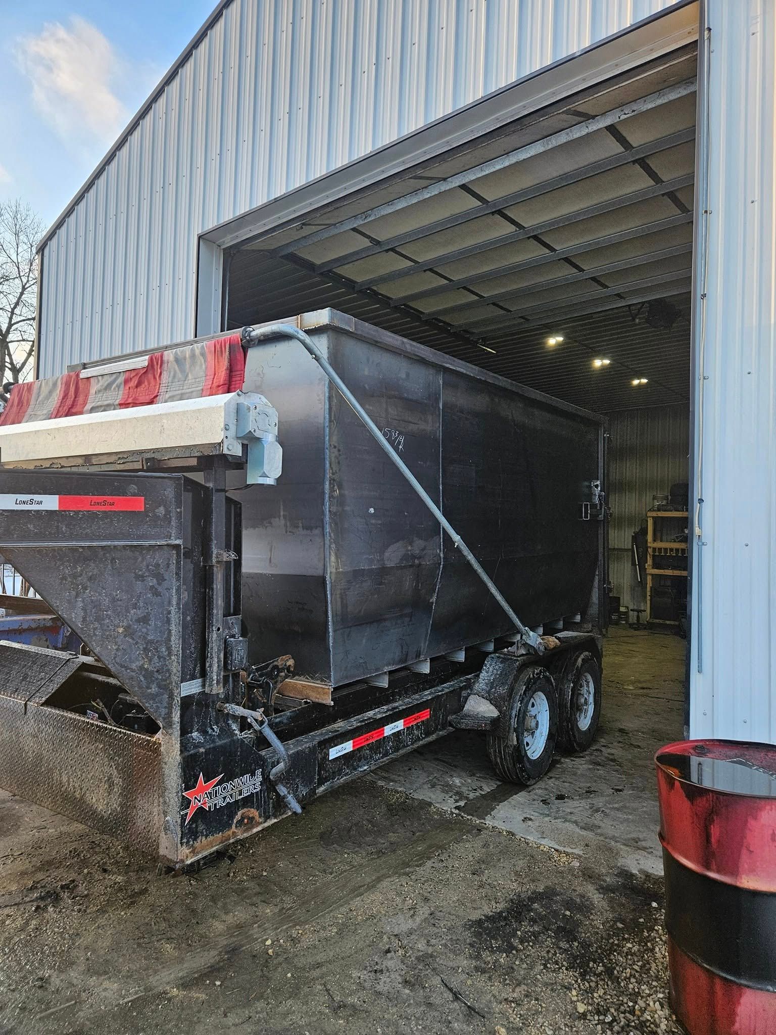 Black dump trailer being loaded into a metal-sided warehouse bay