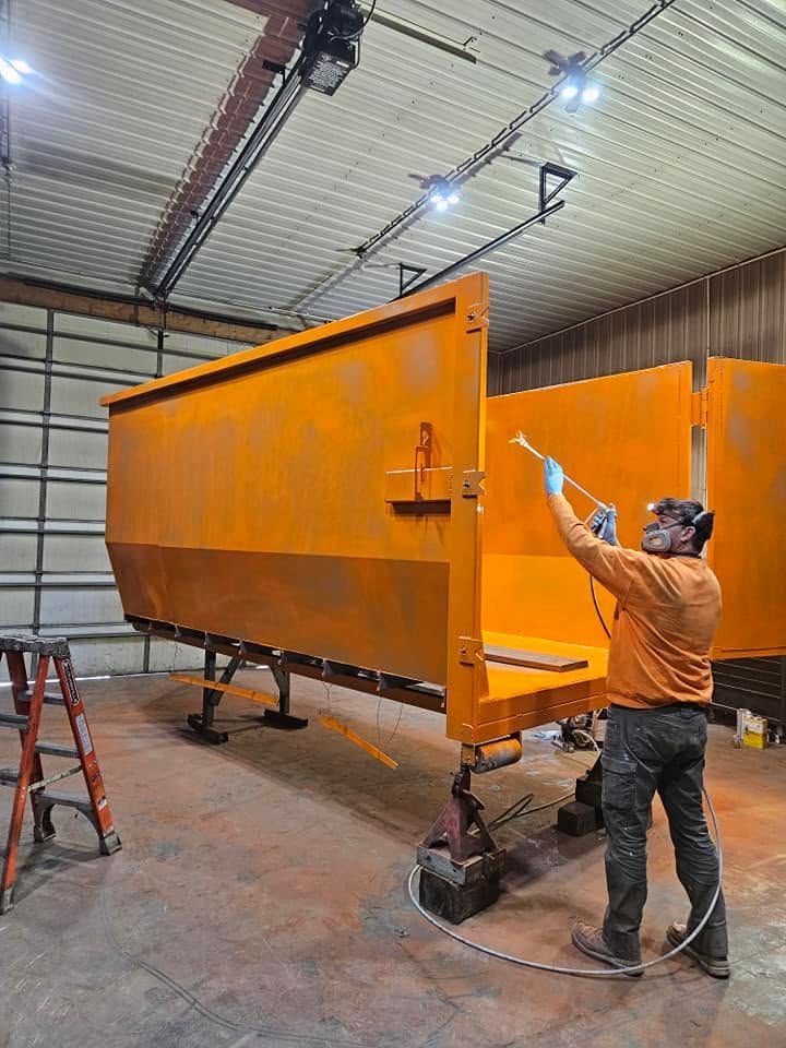 Worker spray-painting a large orange industrial trailer in a workshop