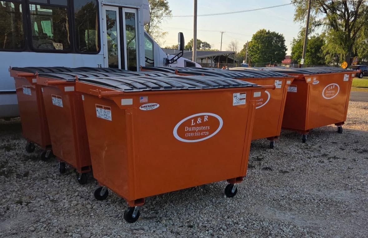 Orange dumpsters lined up on gravel outside a building at dusk