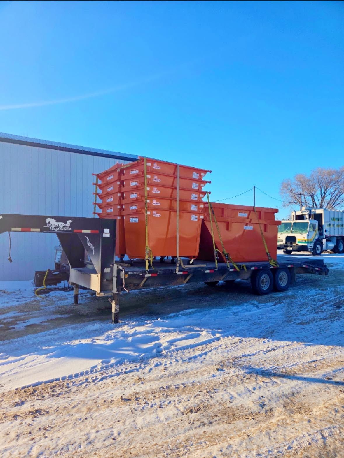 Orange industrial trailer with stacked crates in a snowy lot under a clear blue sky
