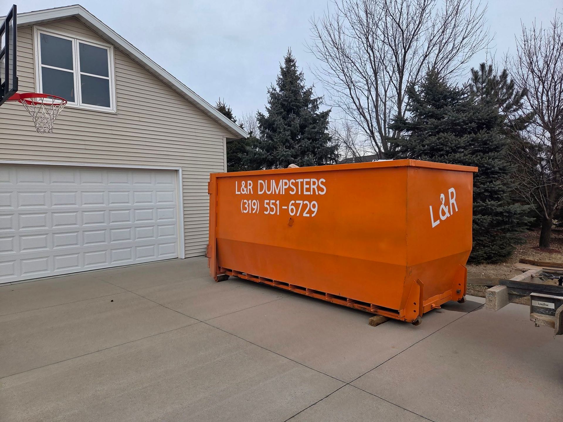 Orange dumpster on a driveway beside a beige house and garage.