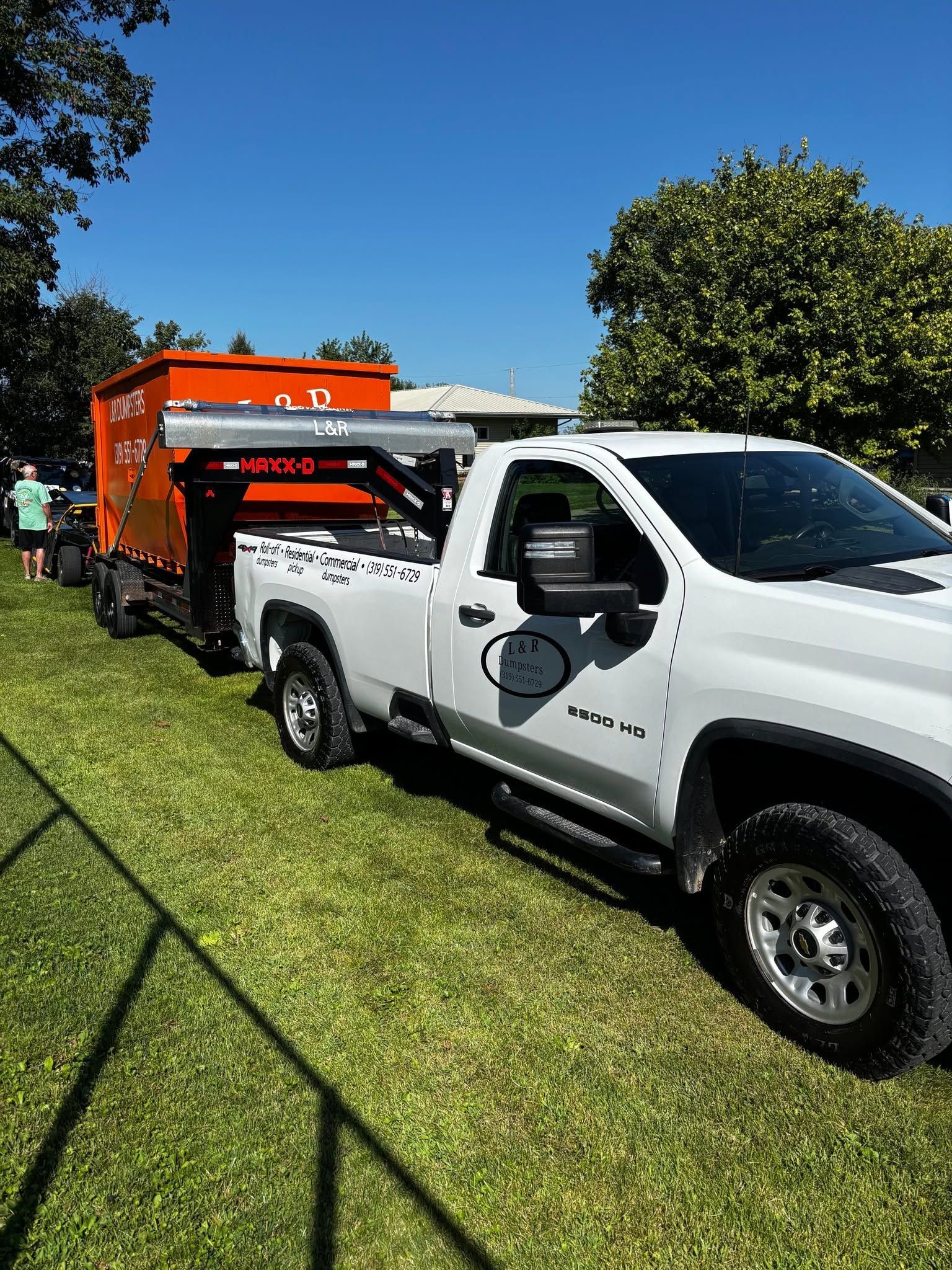 White pickup truck towing an orange utility trailer on a grassy field under a clear blue sky
