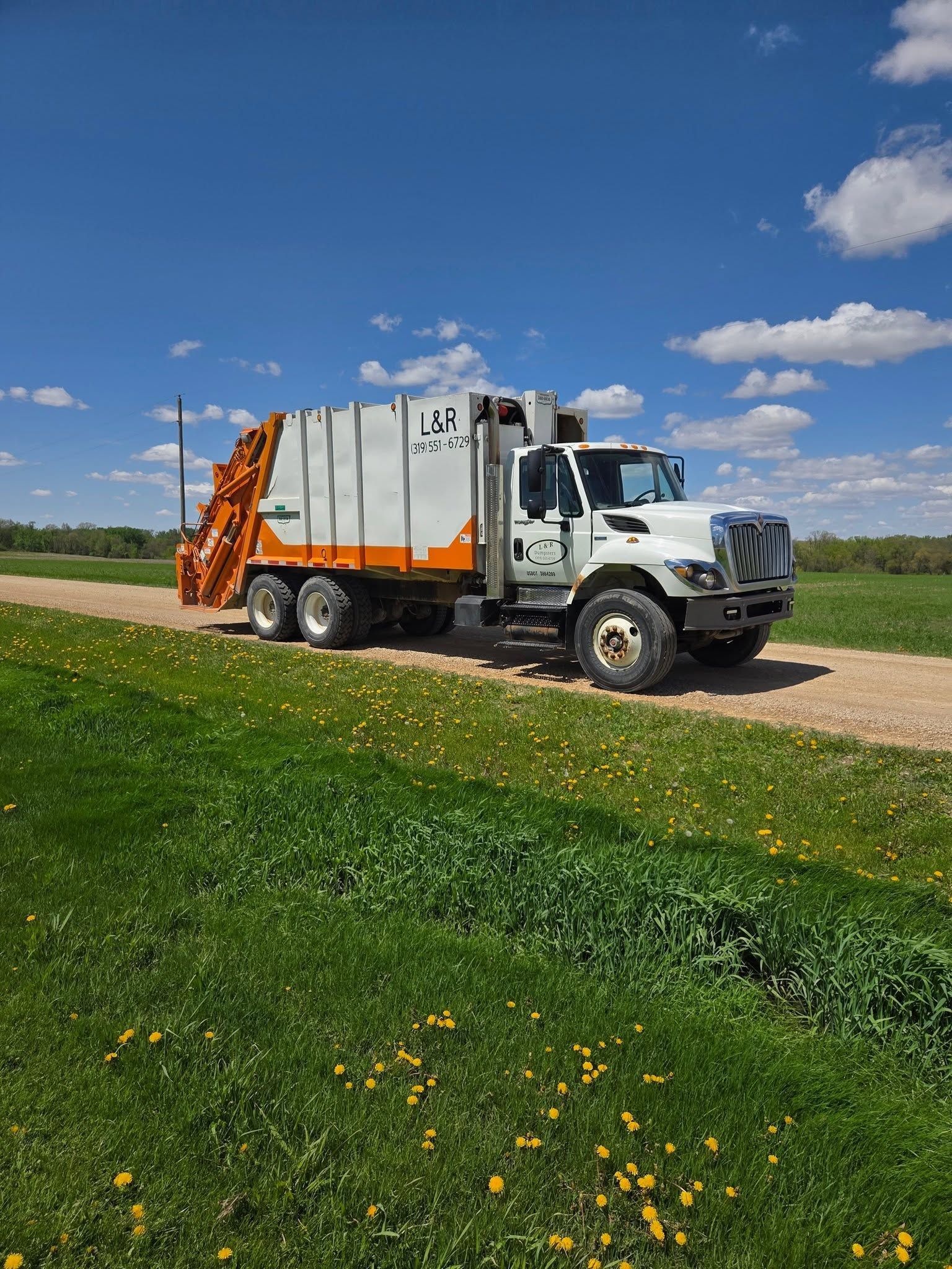 White truck with orange equipment parked on a rural dirt road under a blue sky with clouds.