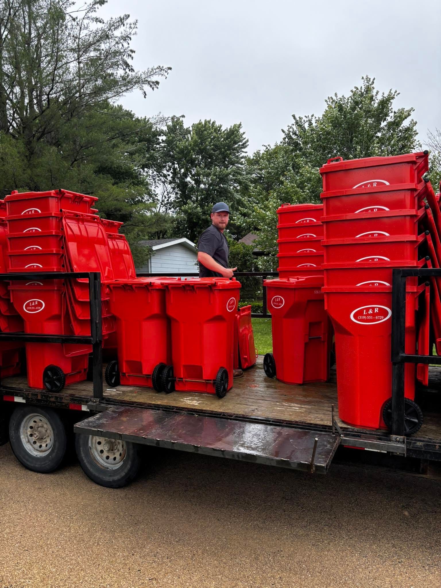Worker beside stacked red garbage bins on a trailer outdoors under cloudy skies