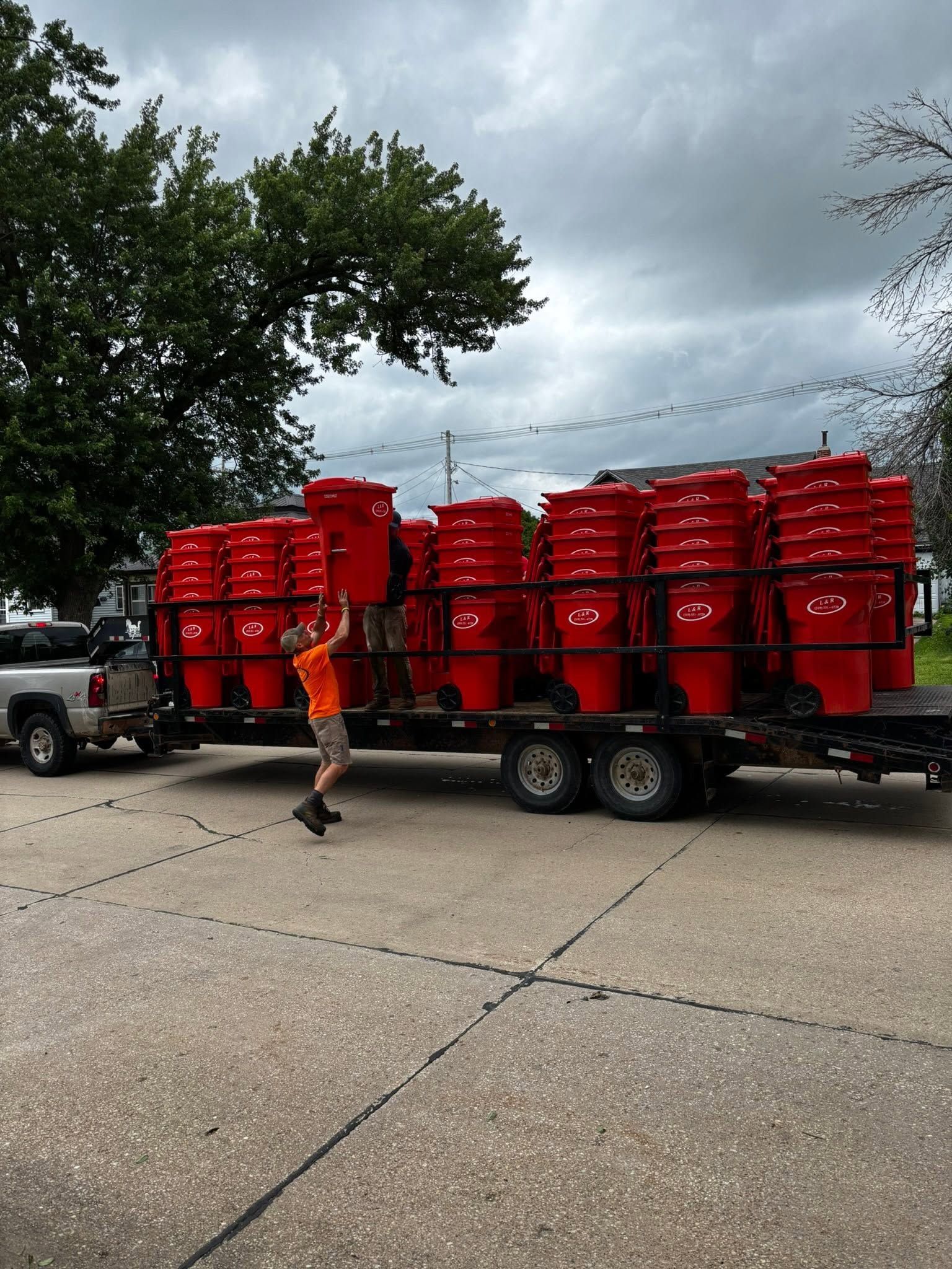 Truck trailer loaded with rows of bright red barrels on a roadside, with a person walking nearby.