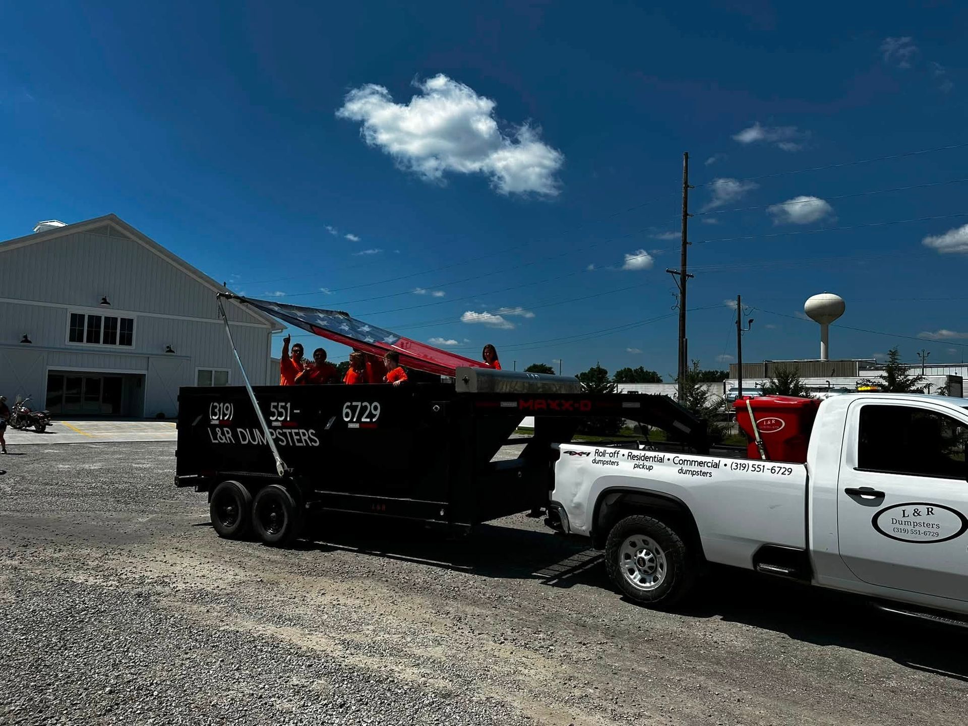 White pickup towing a black dump trailer in a gravel lot under a bright blue sky