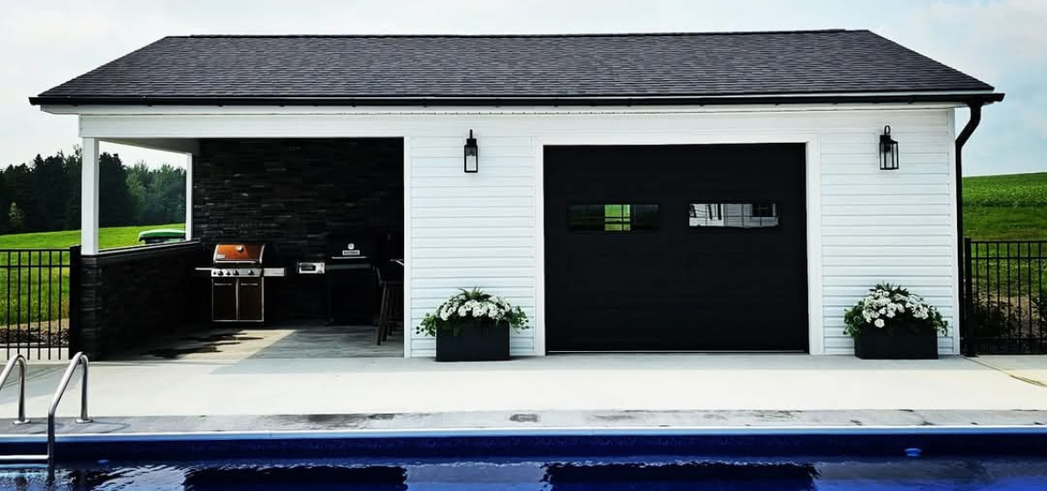 A white garage with a black door is next to a pool