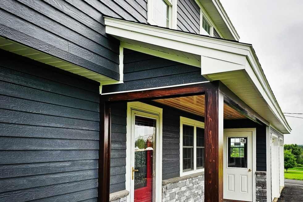 A black house with a red door and a porch.