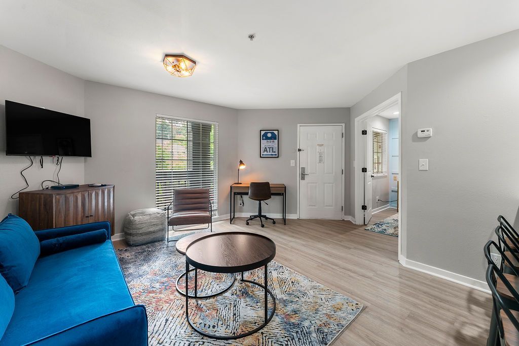 Bright living room with blue sofa, wall-mounted TV, round coffee table, and sliding glass door to a balcony.