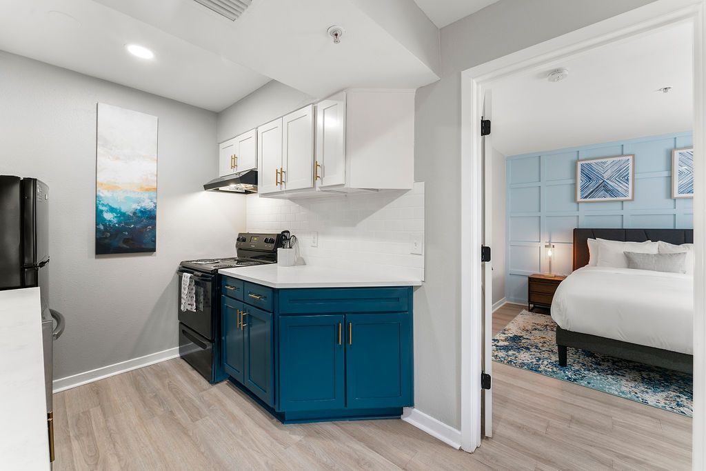Bright apartment hallway with blue kitchen cabinets and an open doorway to a bedroom
