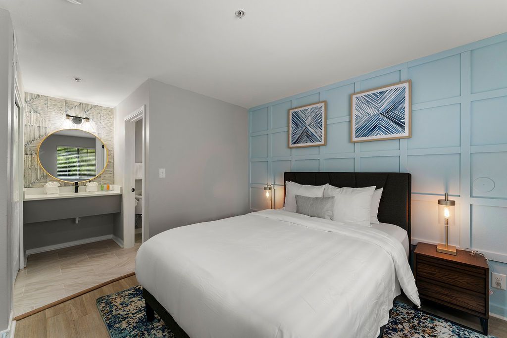 Bright bedroom with white bed, blue paneled wall, and vanity nook with round mirror