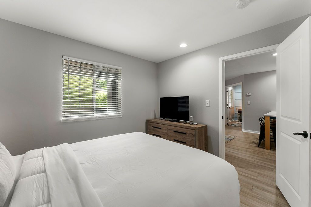 Bright bedroom with a bed, window, TV on dresser, and open door to a hallway