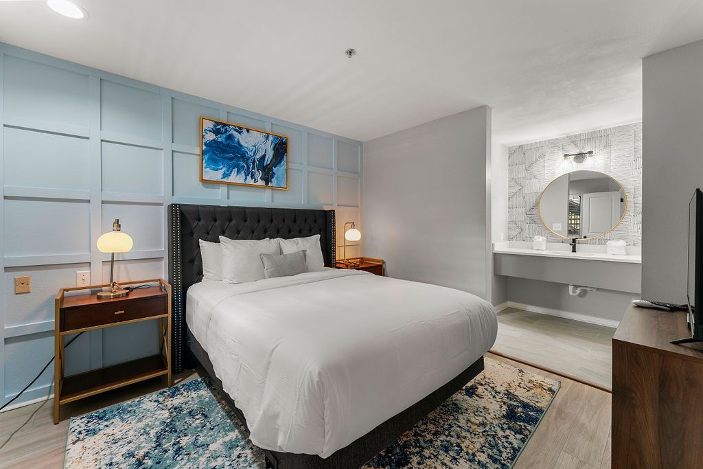 Modern bedroom with a bed, blue accents, nightstands, and a vanity mirror in a bright room