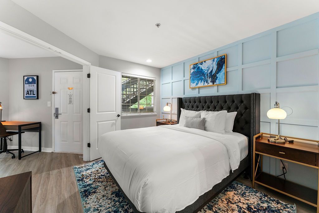 Bright bedroom with blue paneled walls, white bed, patterned rug, and a desk by the window
