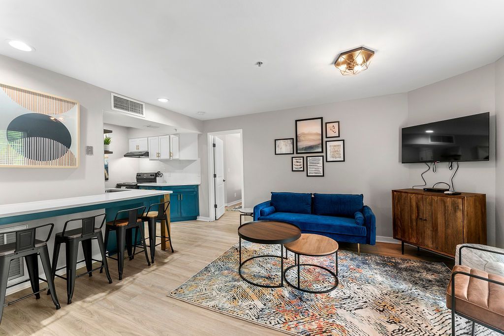 Modern living room with blue sofa, patterned rug, bar stools, wood console, and wall-mounted TV