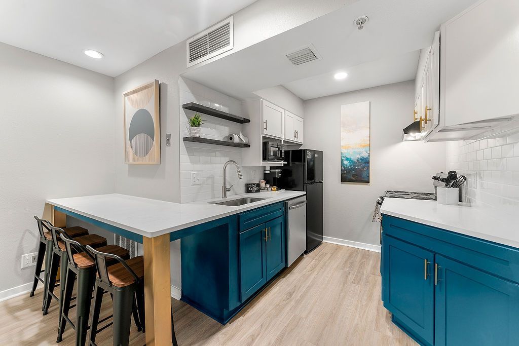 Bright modern kitchen with blue cabinets, white counters, bar stools, and stainless-steel appliances