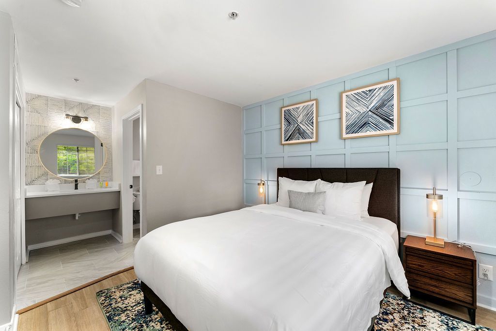 Bright bedroom with a white bed, blue paneled accent wall, and a vanity by an arched window and mirror