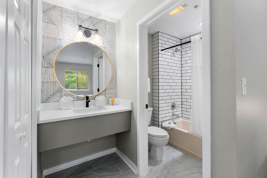 Bright bathroom with vanity, round mirror, and tiled shower and toilet area
