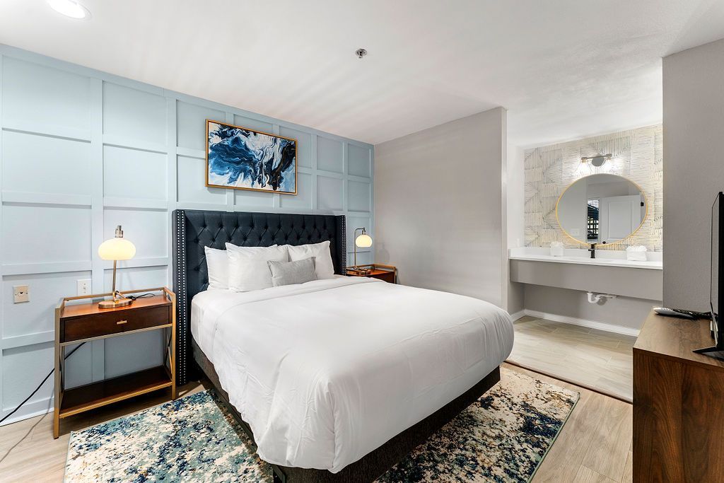 Modern bedroom with blue paneled wall, white bed, bedside lamps, and patterned rug