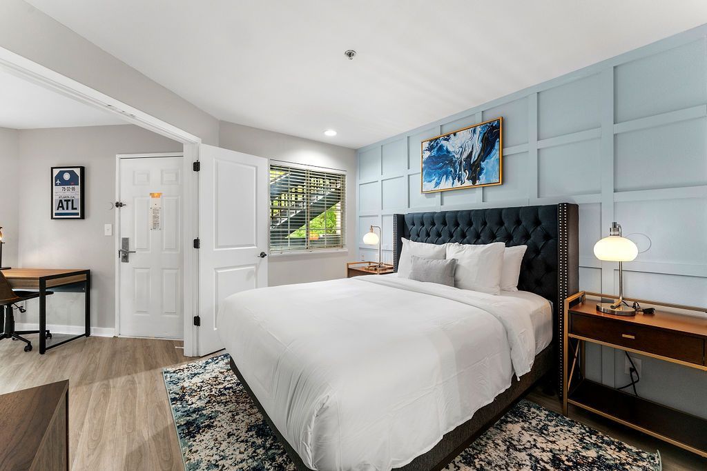 Bright bedroom with a large white bed, tufted headboard, blue wall panels, and framed wall art.