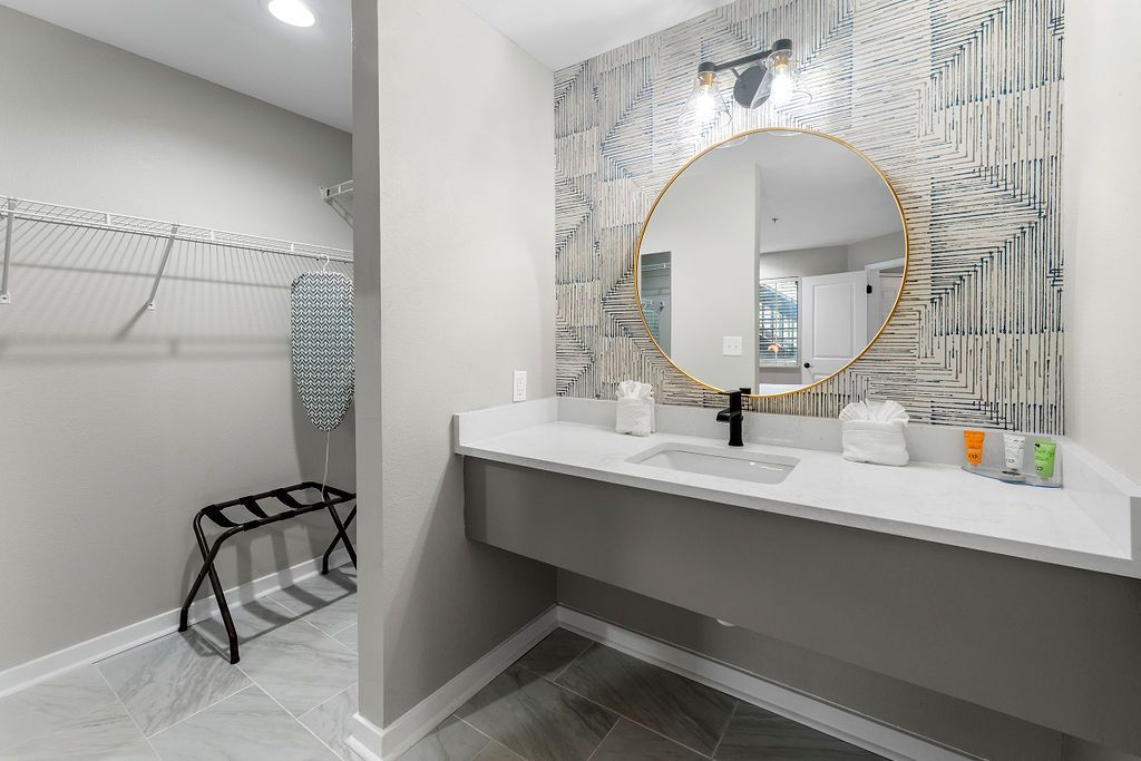 Modern bathroom vanity with round mirror, gray patterned wall, and adjacent walk-in shower area